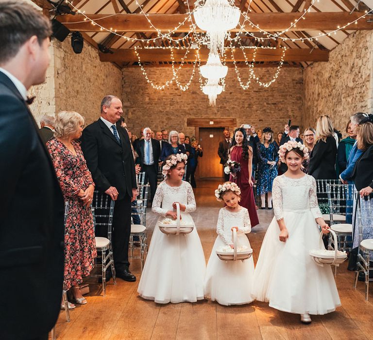 Flower girls in white lace long sleeve dresses with pink rose flower crowns holding basket full of flower petals 