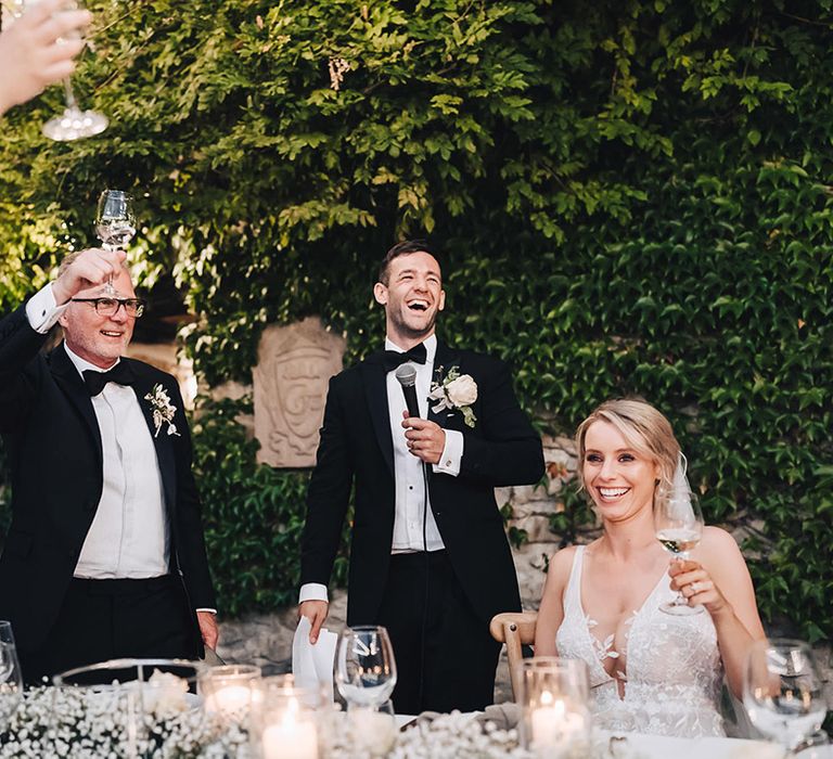 Groom in black-tie gives wedding speech during outdoor Italian reception with winding tables