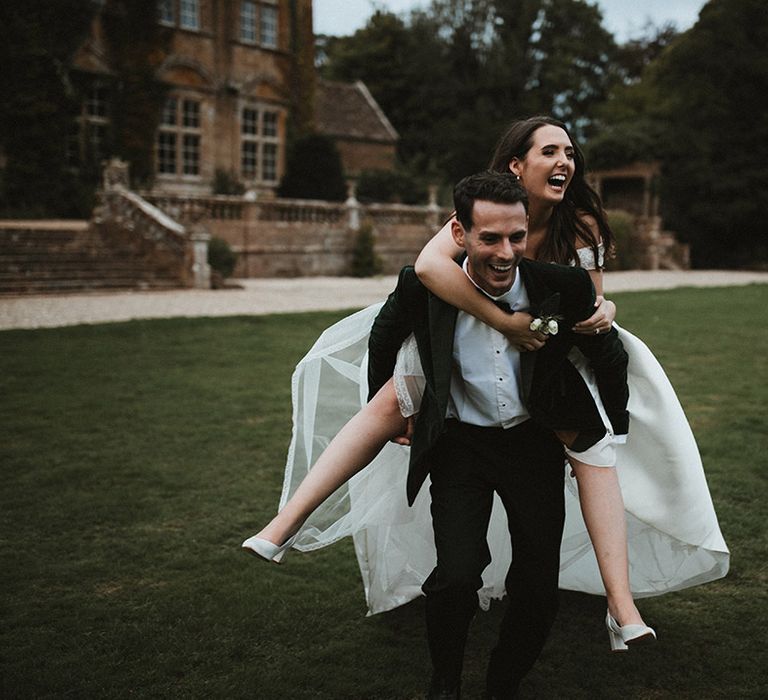 The groom lifts the bride onto his back as they pose for cute couple portraits 