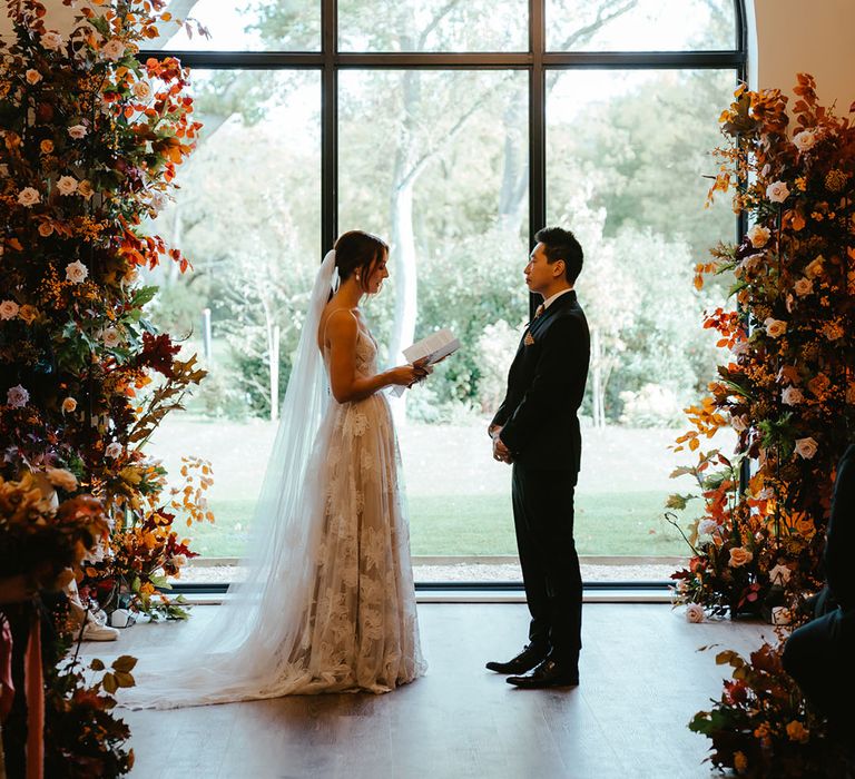 Bride & groom read personal wedding vows beside burnt orange column flowers during ceremony  