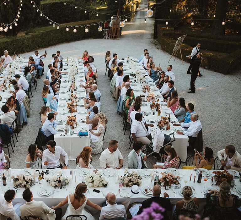 Banquet tables with white tablecloths surrounded by Festoon lighting for outdoor wedding reception in Tuscany