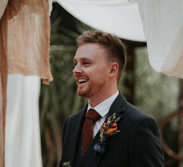 Groomsmen in dark grey suit, burgundy tie and dried flower boutonniere doing wedding speech surrounded by burnt orange and white wedding drapes decorations 