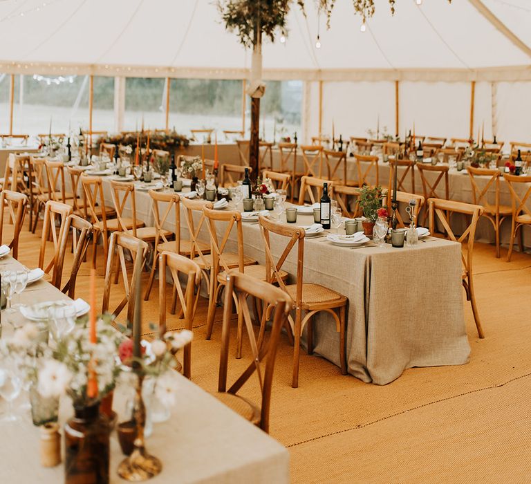 Fairy lights and festoon lights decorate the venue with long banquet tables decorated with potted plants, green glassware and autumnal taper candles 