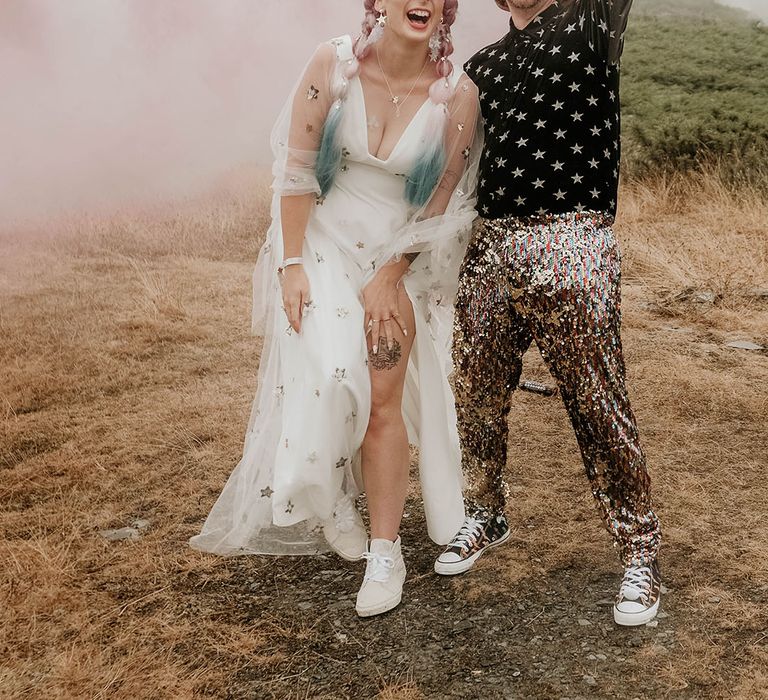 Groom in star patterned shirt with sequin trousers with cowboy hat groom accessory waving a pink smoke bomb with the bride in a star printed wedding dress 