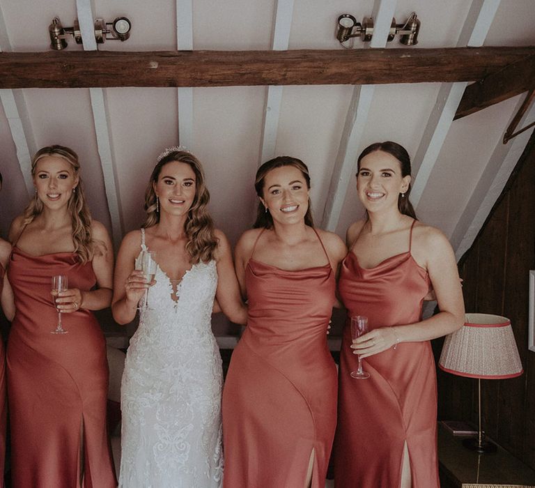 Bridesmaids in coral and peach cowl neck satin bridesmaid dresses with the bride in a fitted lace wedding dress with glittery tiara 