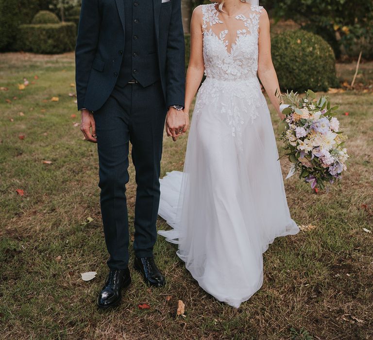 Groom smiling at the bride in a three piece navy suit and the bride in an illusion lace wedding dress with pretty pastel bouquet 