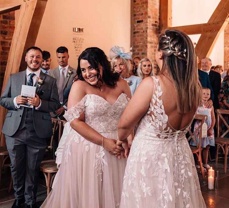 LGBTQIA+ wedding with the two brides holding hands and smiling with silver hair accessories and lace wedding dresses