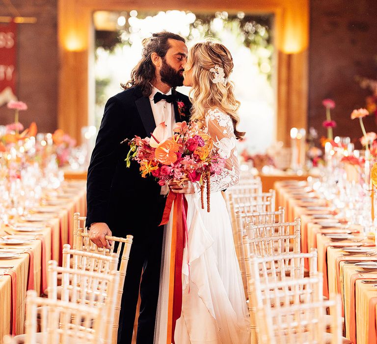 Groom in black tie kisses the bride in a long sleeve white wedding dress at their wedding reception 