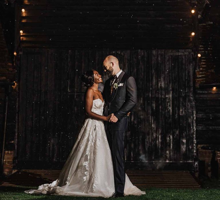 Groom in classic black three piece grooms suit with bow tie and white rose and foliage boutonniere in church standing with bride in sweetheart neckline lace wedding dress outside of Lains Barn 