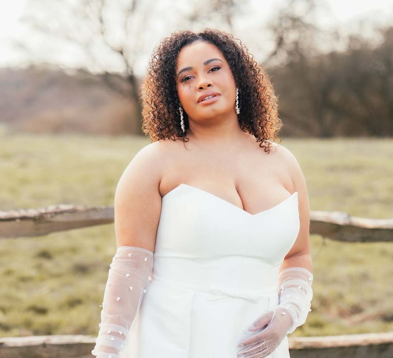 Bride in strapless wedding dress with front slit, puddle train and mesh pearl gloves holding orange, lilac and peach mixed flower bridal bouquet 