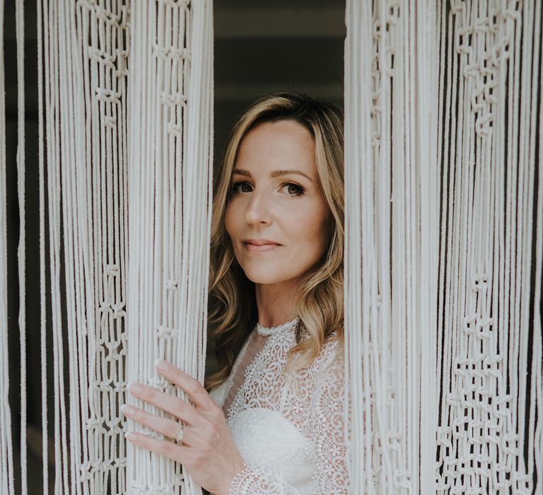 boho bride in a lace wedding dress peeking through macrame curtains