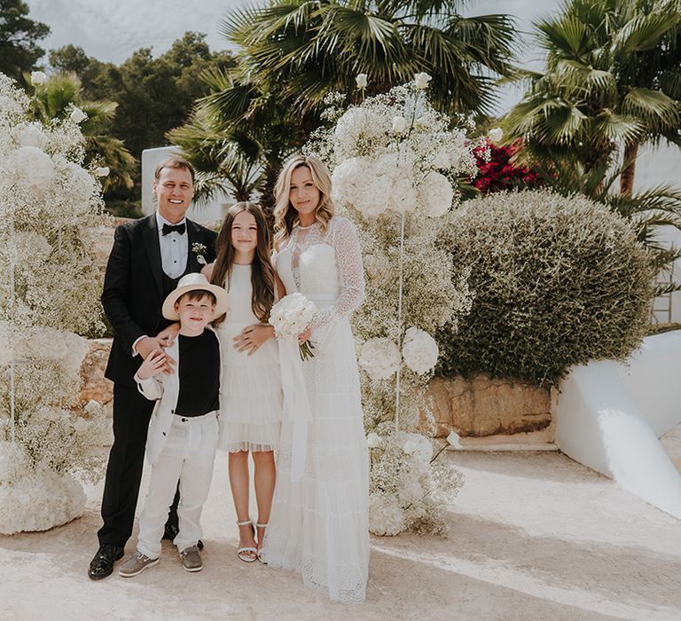 family portrait at pure house ibiza wedding with white gypsophila column flowers bride in lace wedding dress groom in a tuxedo and children in monochrome outfits