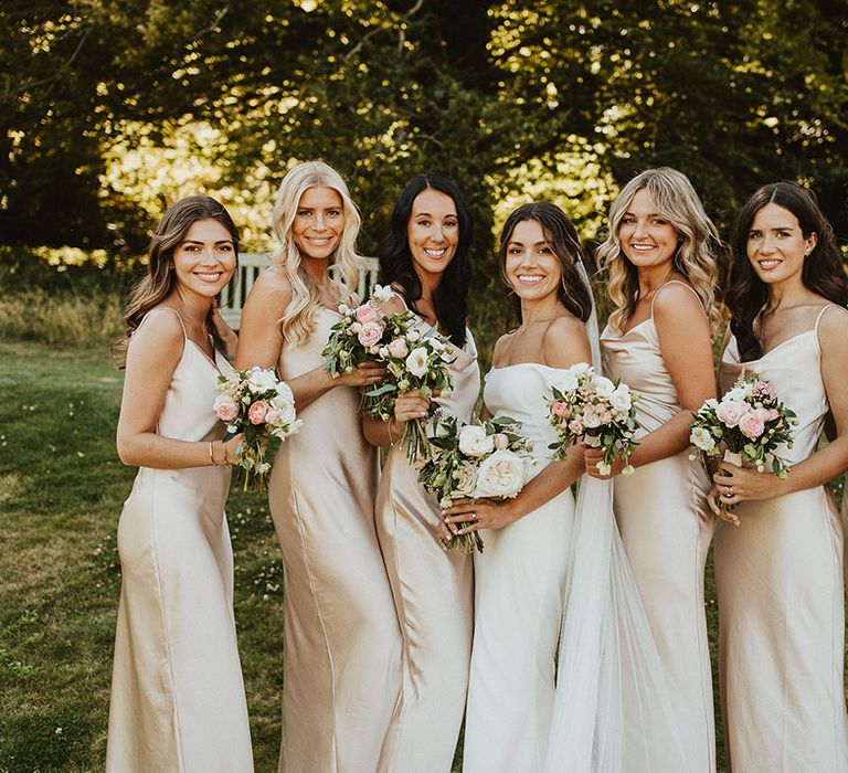 Bridesmaids in satin cowl neck gold bridesmaid dresses smiling with the bride in an off the shoulder gown