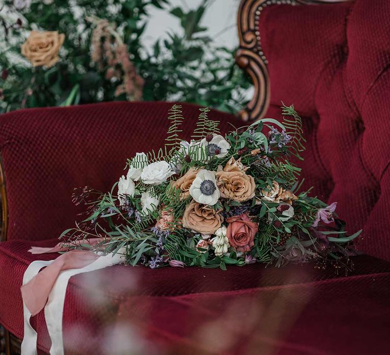 Dried wildflower bridal bouquet tied with neutral and dusky pink ribbon on maroon loveseat wedding furniture at Buxted Park 