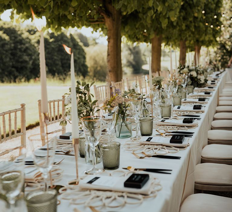 Gold rimmed wine glasses, green coloured glassware, white taper candles, with festoon lighting for outdoor wedding breakfast 