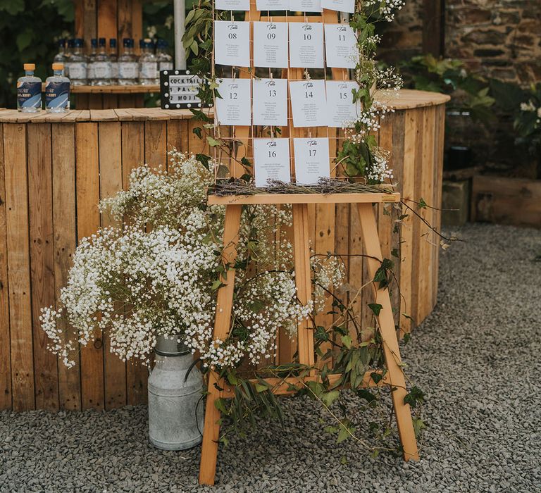 Foliage and gypsophila decorating the wooden seating chart and table plan sign next to the bar 