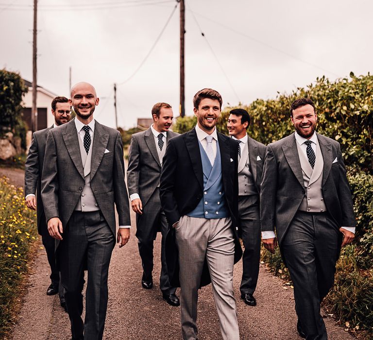 groom in a blue double breasted waistcoat and grey morning suit walking through Sennen Cove streets with his groomsmen