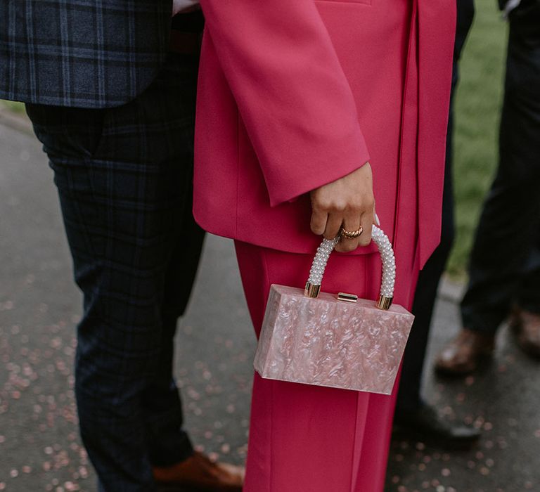 Groomswoman wearing hot pink suit carrying a light pink quartz style clutch 