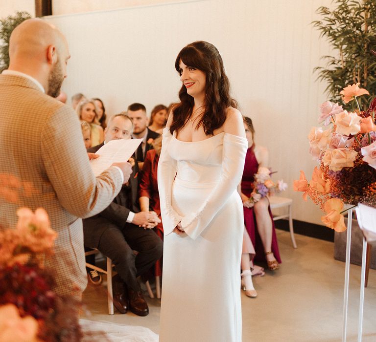 Groom reads out his wedding vows to the bride in an off the shoulder long sleeve wedding dress 