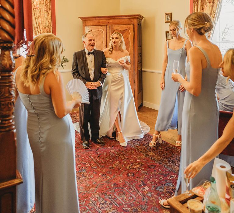 Father of the bride in a black tuxedo walks with the bride in an off the shoulder wedding dress 