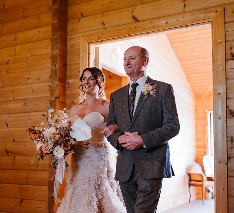 Father of the bride in a grey wedding suit walks the bride in a Recycle My Wedding pre-loved wedding dress down the aisle 