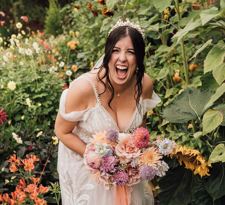 Laughing bride wearing lace wedding dress with princess skirt carrying colourful wedding bouquet 