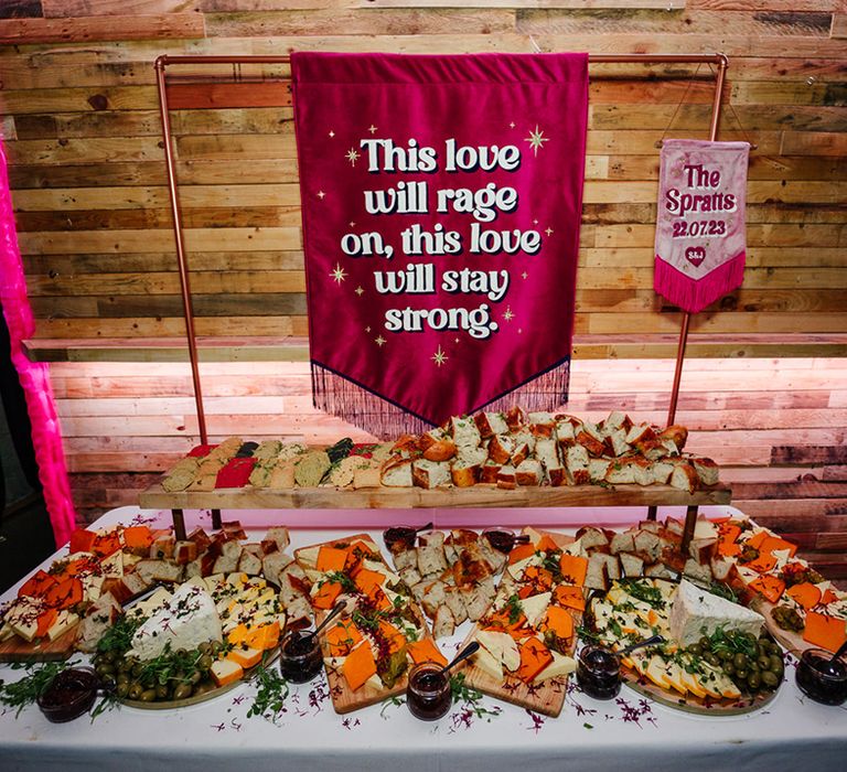 Dark pink tassel retro wedding banner signage as backdrop to grazing table 