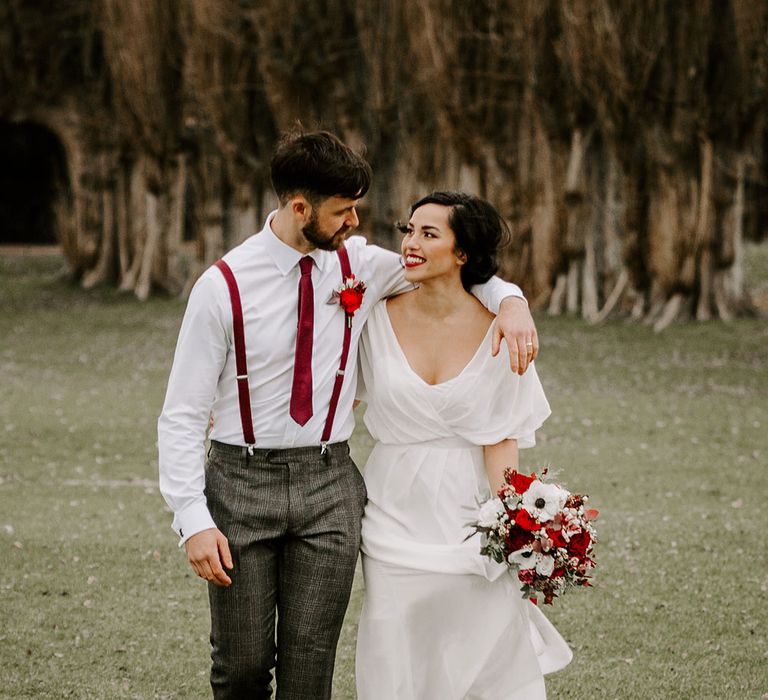 Smiling Bride and Groom with red floral bouquet walk in park