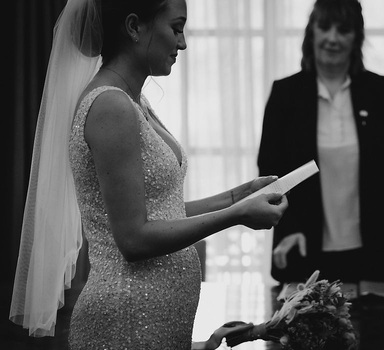 Pregnant bride reading her wedding vows at intimate wedding 