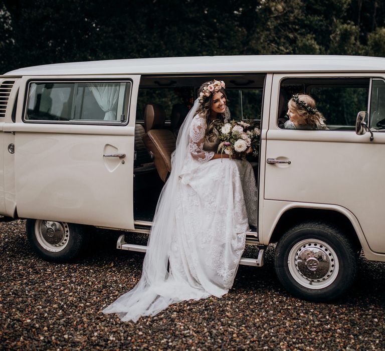 Boho bride with white rose bouquet and pink rose flower crown sits in vintage VW wedding van