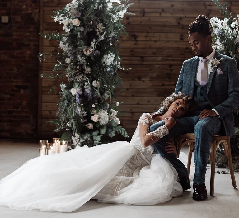 Bride and groom sit in front of their romantic wedding flowers in a rustic exposed brick barn