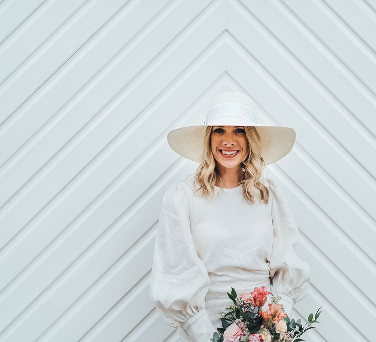 Bride wearing puff sleeve wedding dress with wedding hat holding pink and coral floral bouquet 