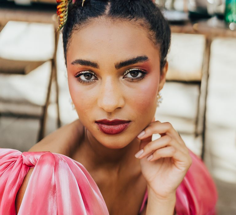 A Black bride looks to camera wearing a pink dress and wearing a large flower crown.