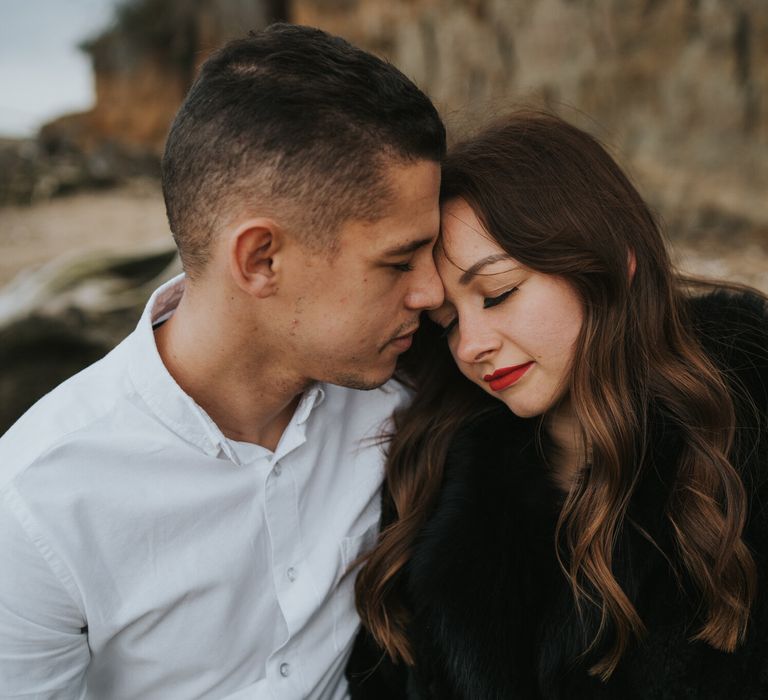 Groom-to-be kissing his Fiancee's head with long wavy brunette hair, red lipstick and a black faux fur coat