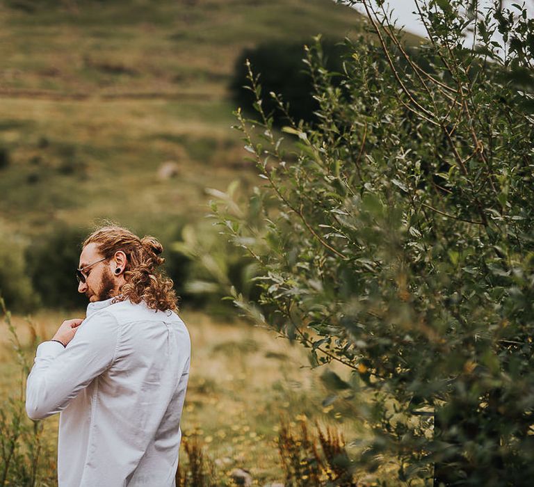 Long haired groom does shirt up before ceremony