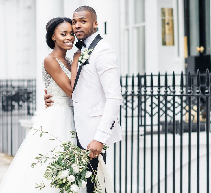 Bride leans into groom whilst he holds white floral bouquet