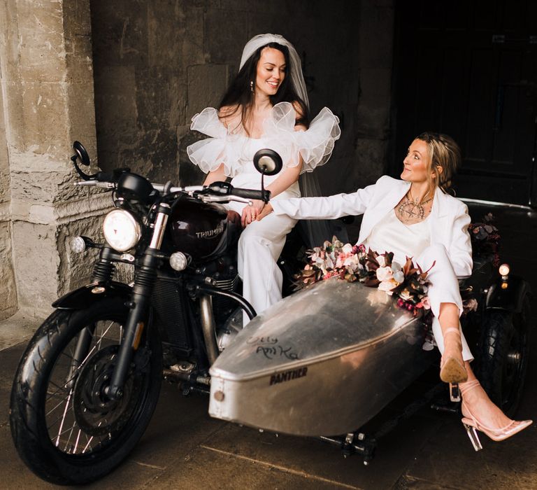 Bride in a trousers suit with jacket and clear block heel shoes resting her feet over the edge of the motorbike sidecar