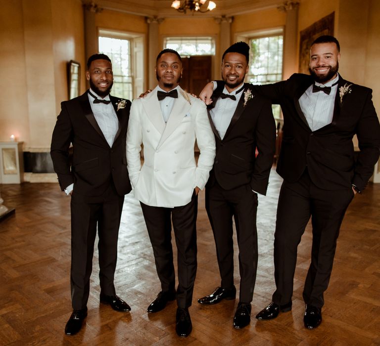 Groom in a white tuxedo jacket with his groomsmen in black tie suits 