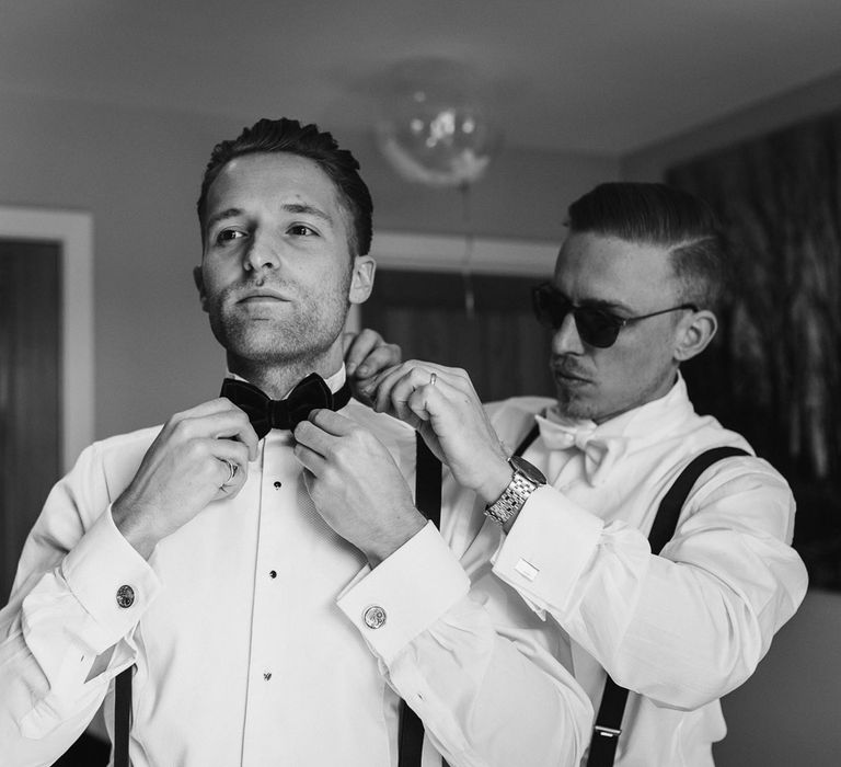 Groomsman and groom both in white shirts, braces and bow ties getting ready for Caswell House wedding