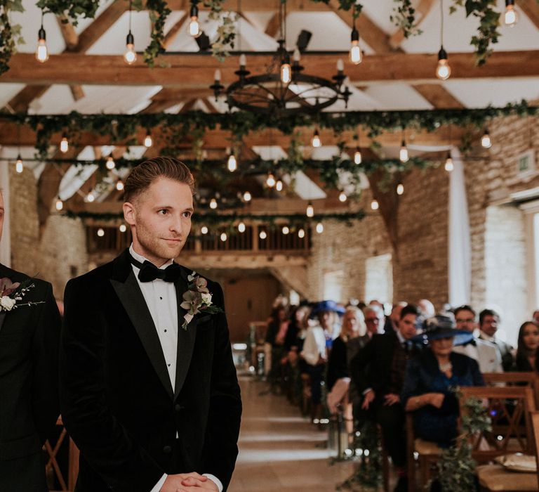 Groom in black velvet Hugo Boss suit stands with best man in black Moss Bros suit at the altar waiting for bride at Caswell House Wedding