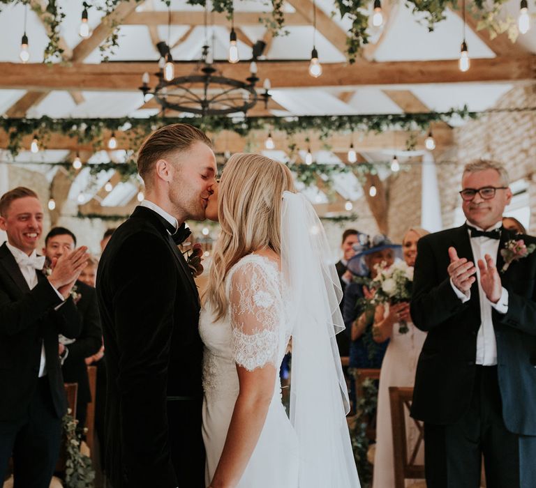 Bride in white Charlie Brear wedding dress and white Augusta Jones lace top and groom in black velvet Hugo Boss suit kiss at the altar at Caswell House wedding