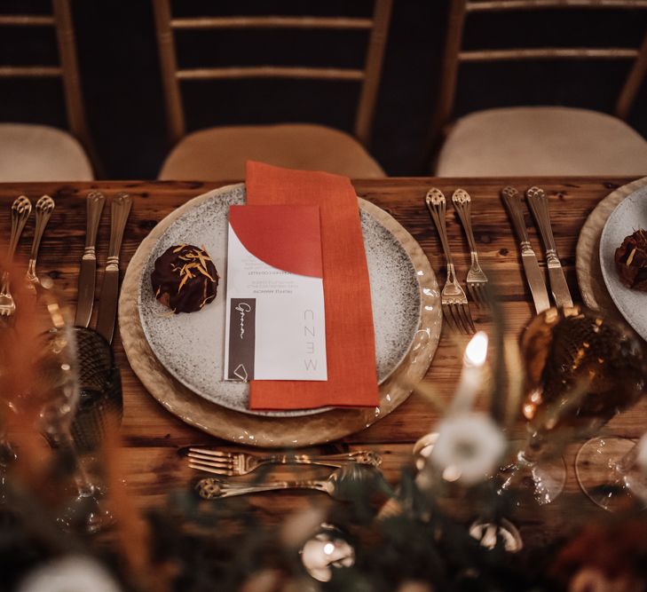 Place setting with gold charger plate and cutlery, patterned tableware and orange napkin 