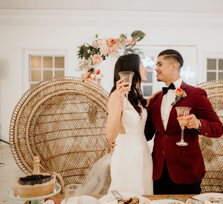 Bride and groom standing at their sweetheart table with wicker peacock chairs