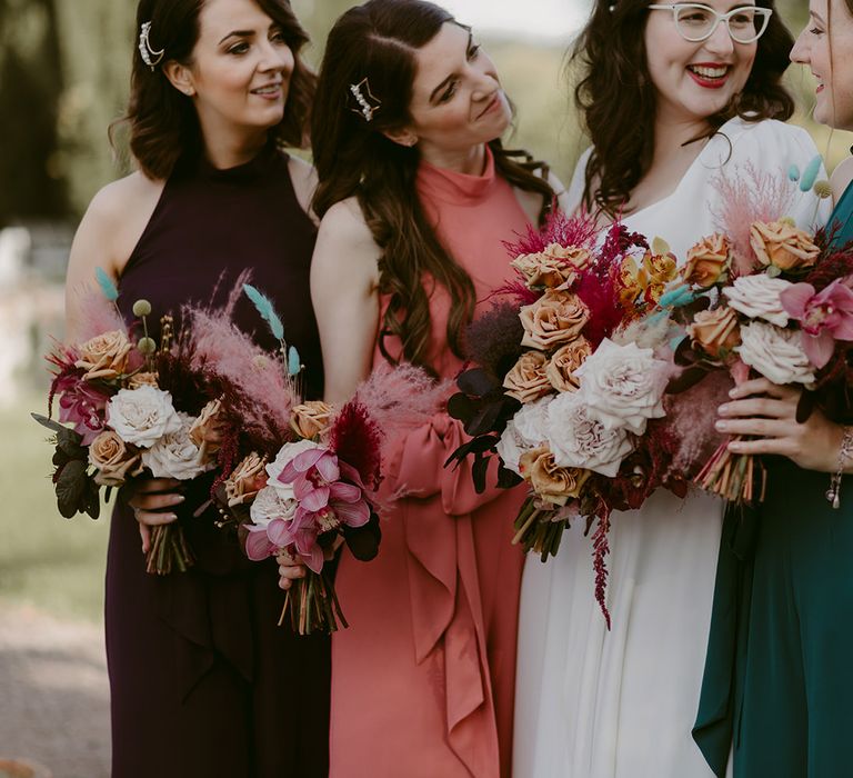 Bride in white Rime Arodaky wedding dress standing with bridesmaids in different coloured Rewritten bridesmaids dresses all holding white and pink rose and pampas grass wedding bouquets