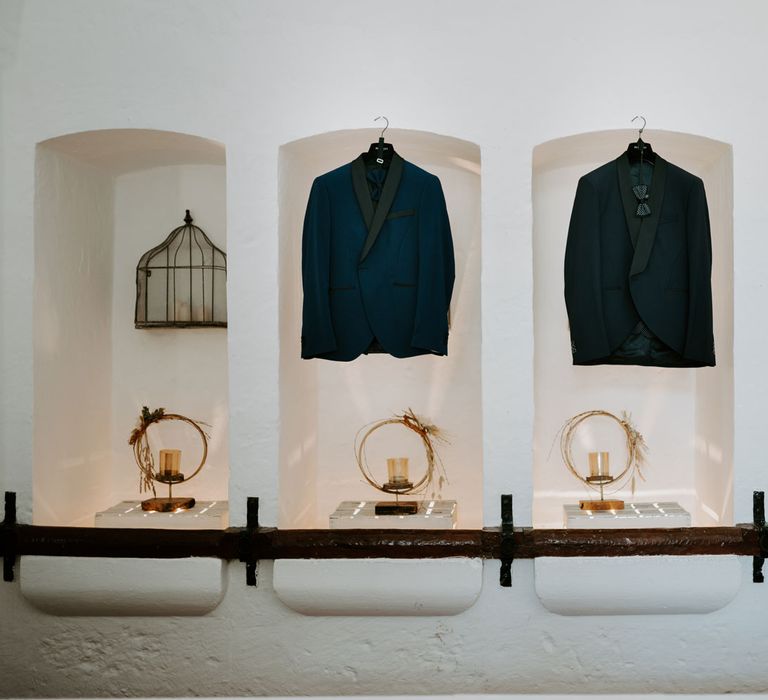 Two navy suit jackets hanging in white stone alcoves lit by candles at enchanted forest wedding in Italy