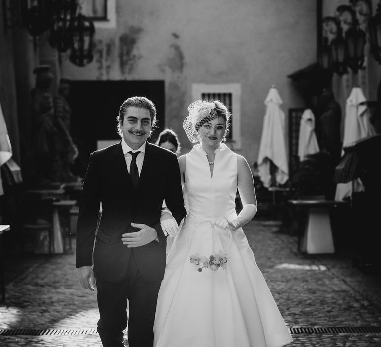 Bride walking down cobbled aisle in Rome wearing 1960s vintage style wedding dress and orchid flower hoop