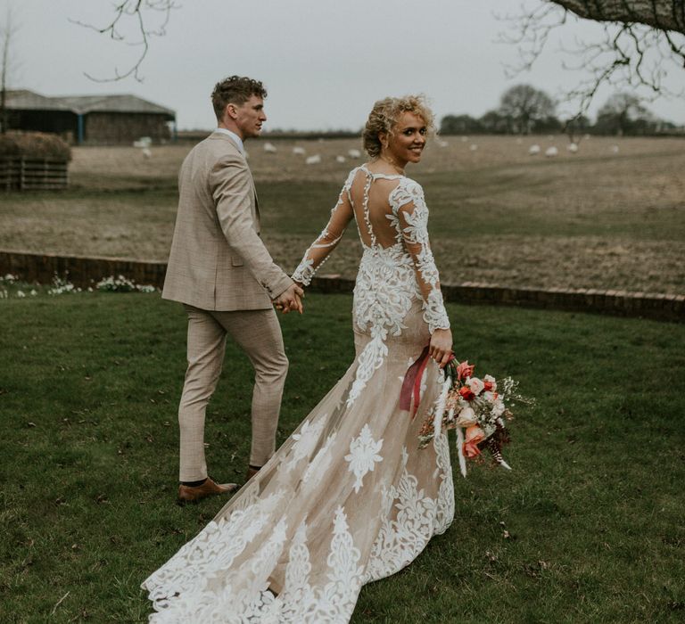 Bride and groom walking hand in hand through Hornington Manor, both with curly hair, the bride is wearing a mesh embroidered wedding dress with tulle train