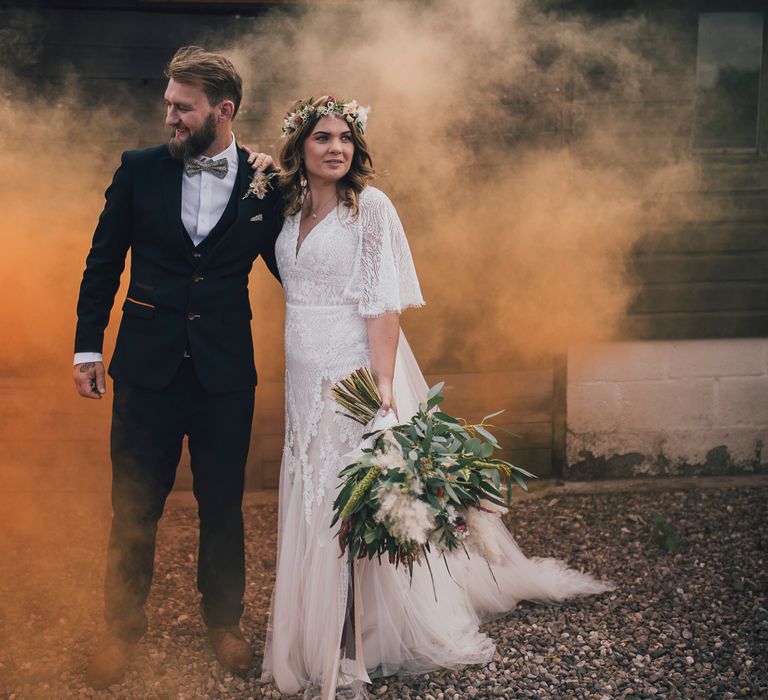 Bride & groom are surrounded by orange smoke as they laugh and smile together