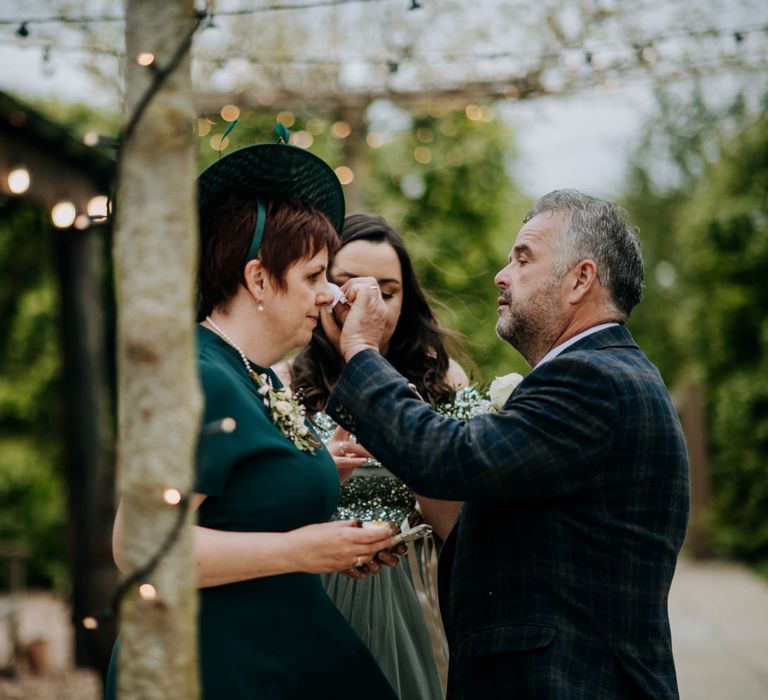 Father of the bride wiping the mother of the brides tears away 