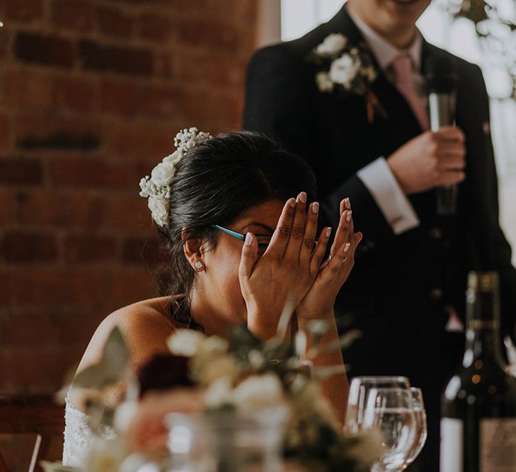 A bride in Sophia Tolli covers her face as she laughs during wedding speeches.